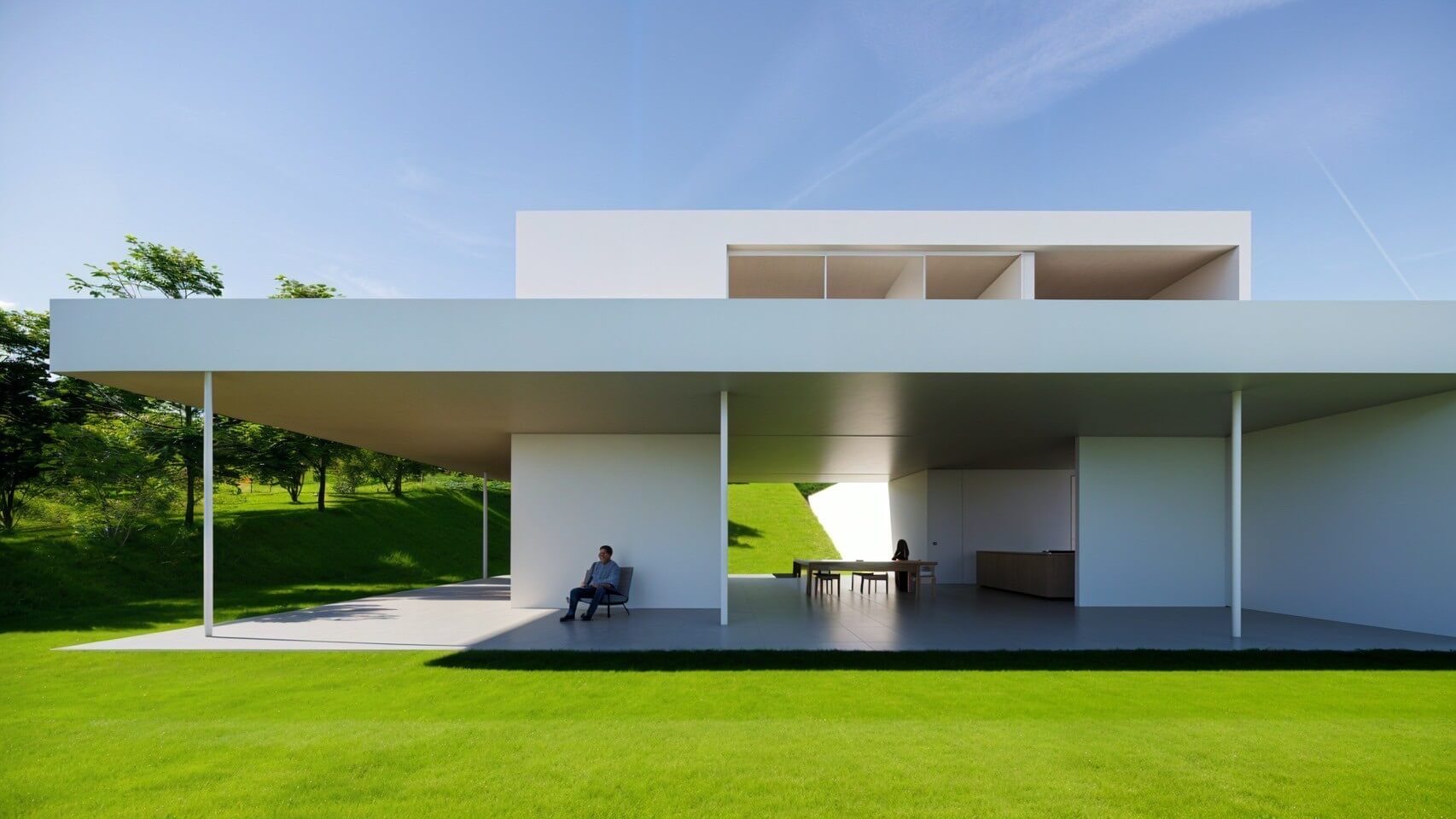 A modern home protected by a large overhang, with someone quietly enjoying the space